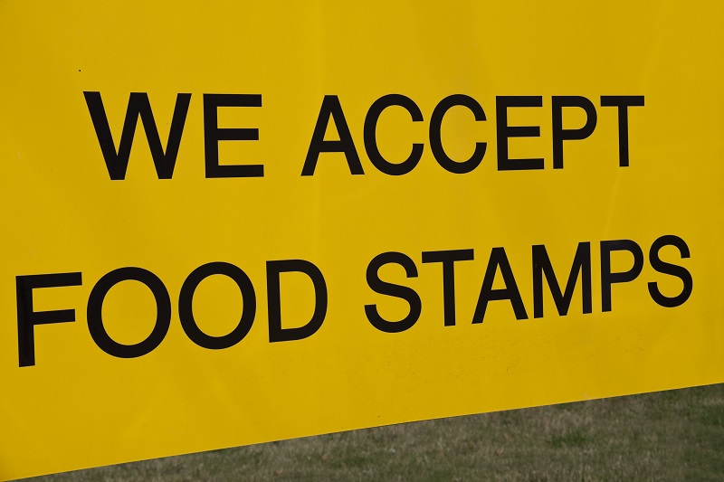 big yellow sign with black letters spelling "we accept food stamps"