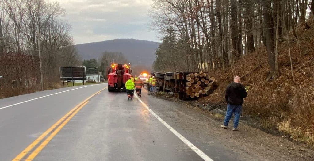 Large truck carrying logs crashes, narrowly misses school bus