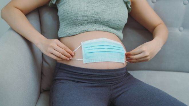 mask to protect against COVID-19 held against a pregnant woman's belly