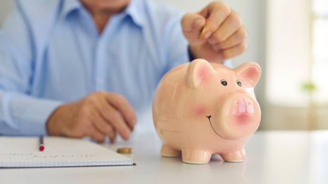 retired man placing money inside of a piggy bank to show savings for a retirement plan, like a 401k