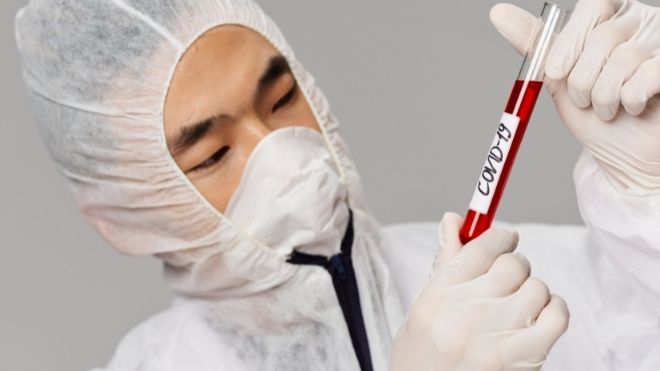 scientist examining a COVID-19 test tube while wearing ppe
