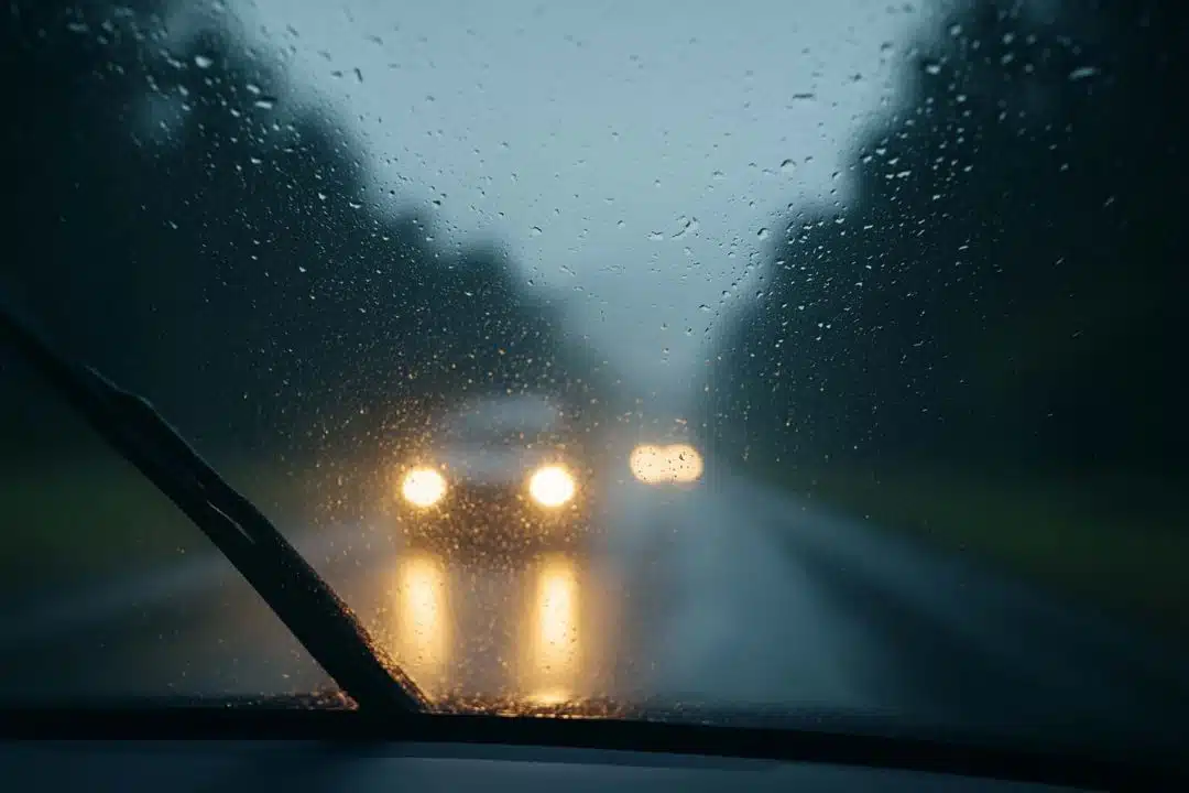 View through a rain-covered windshield with headlights on during rainy conditions, illustrating New York’s headlight and wiper law.