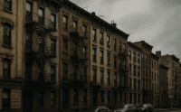 Row of old brick apartment buildings with fire escapes under cloudy skies during the 2025 housing crisis