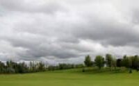 Low gray clouds over a green field and trees